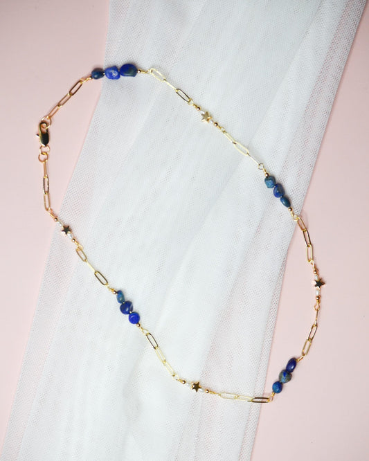 Gold chain necklace with blue lapis lazuli and gold star beads on a white fabric background