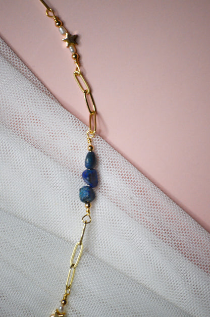 Gold chain necklace with blue beads on a light pink fabric background