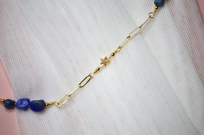 Necklace with blue beads  and gold star beads with small pearl accentsand gold chain on a white fabric background