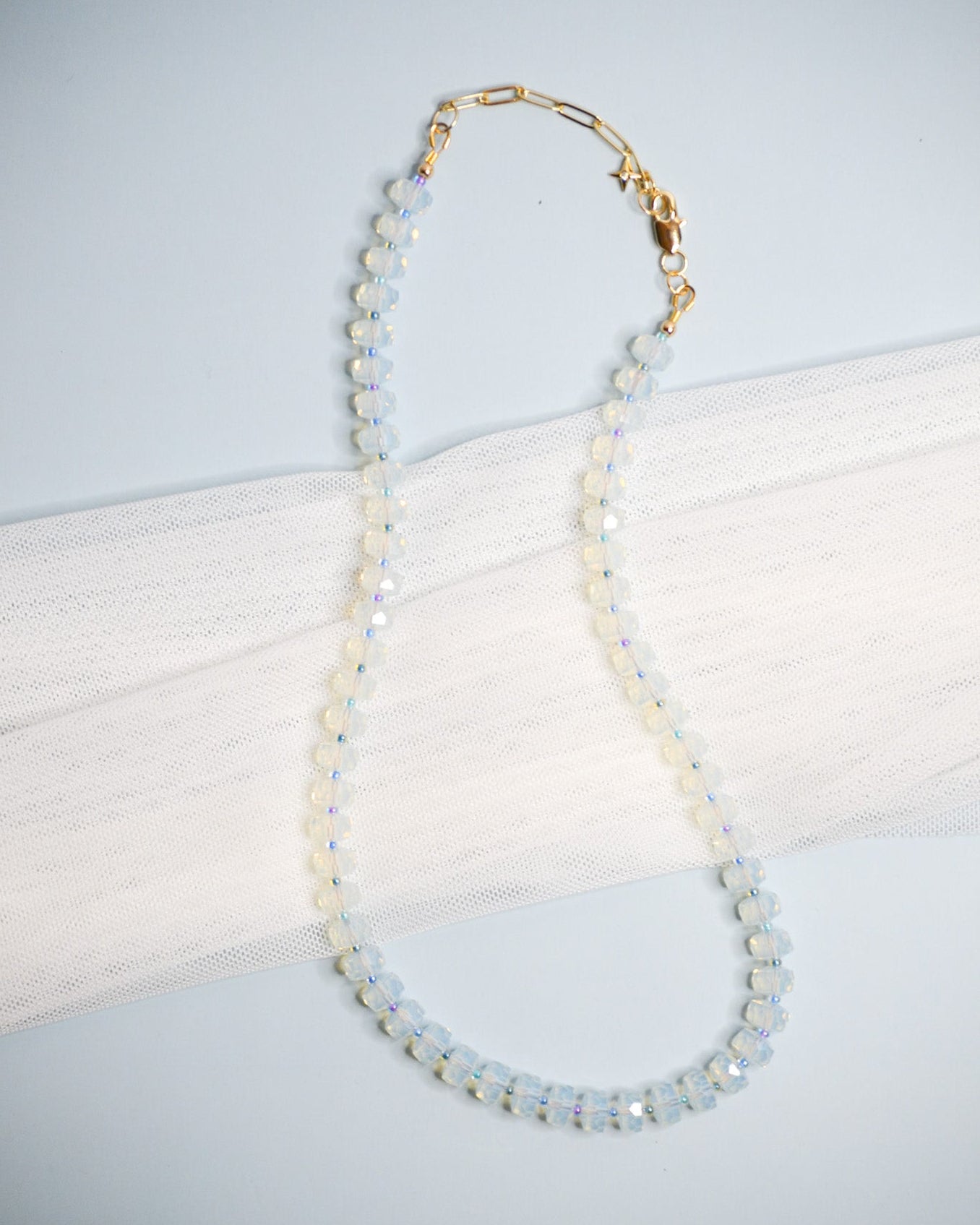 Necklace with opalite beads, small cool toned beads, and gold chain on a light blue background