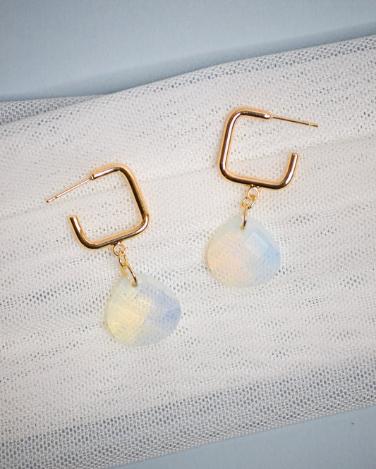 Gold square dangle hoop earrings with opalite stones on a textured white surface