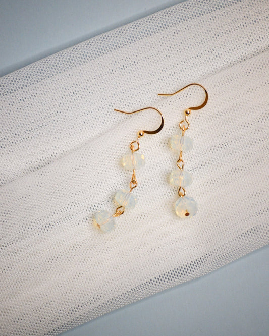 Pair of gold and iridescent beaded dangle earrings on a textured white fabric background