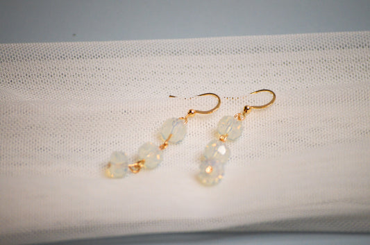 Gold dangle earrings with iridescent stones on a white fabric background