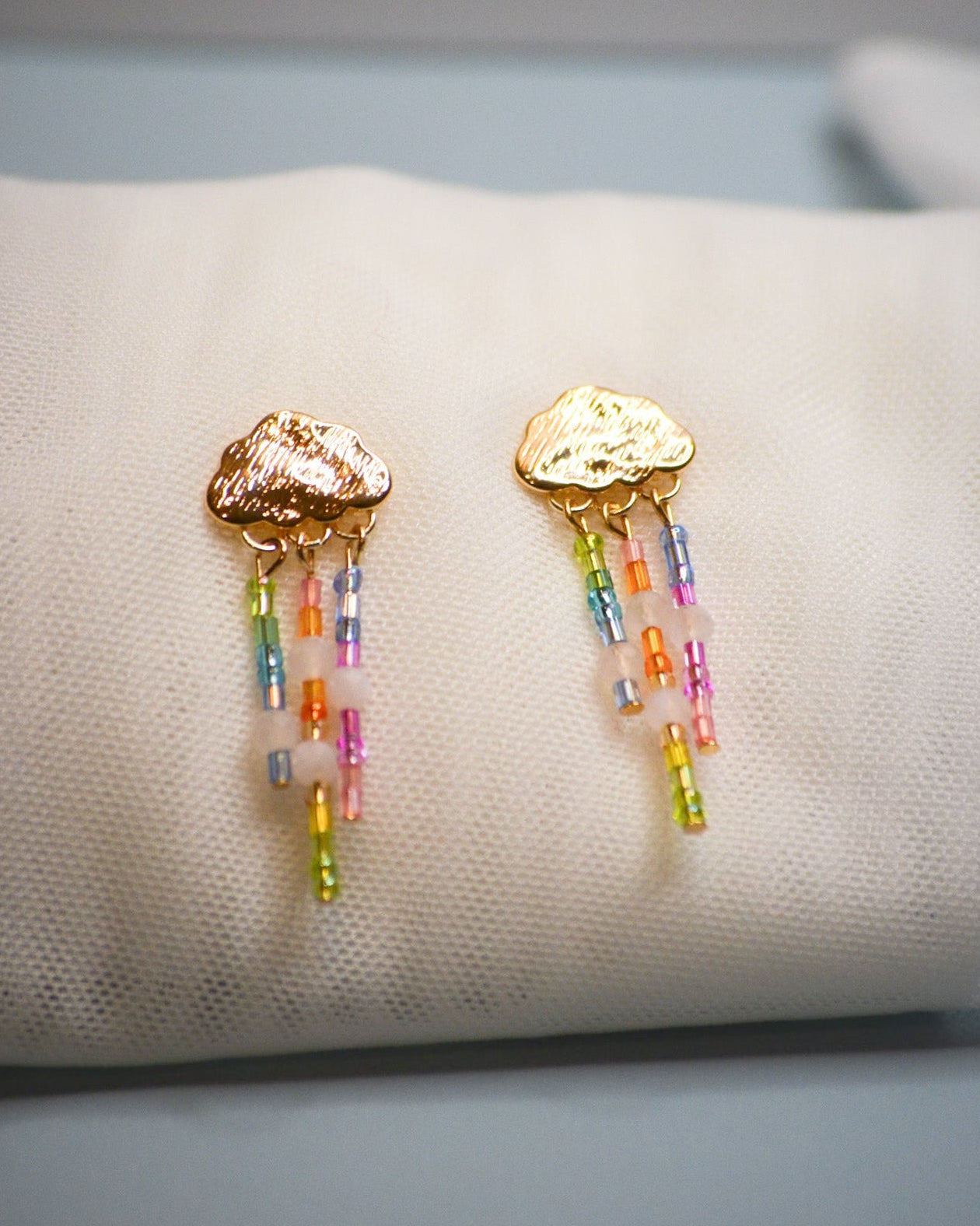 Gold cloud earrings with colorful raining design beads on a white cushion