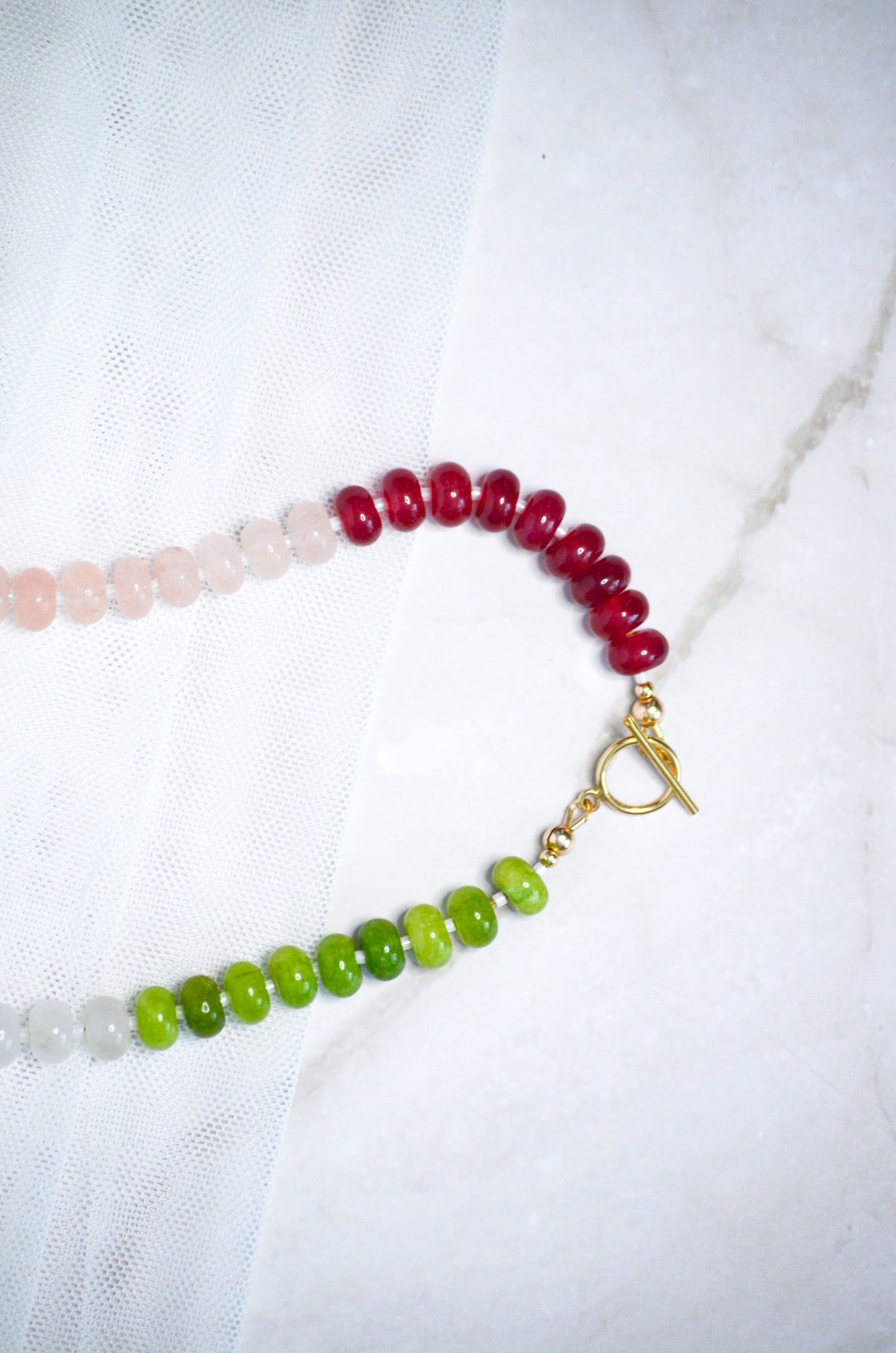 Beaded necklace with red, green, and a gold toggle clasp on a white background