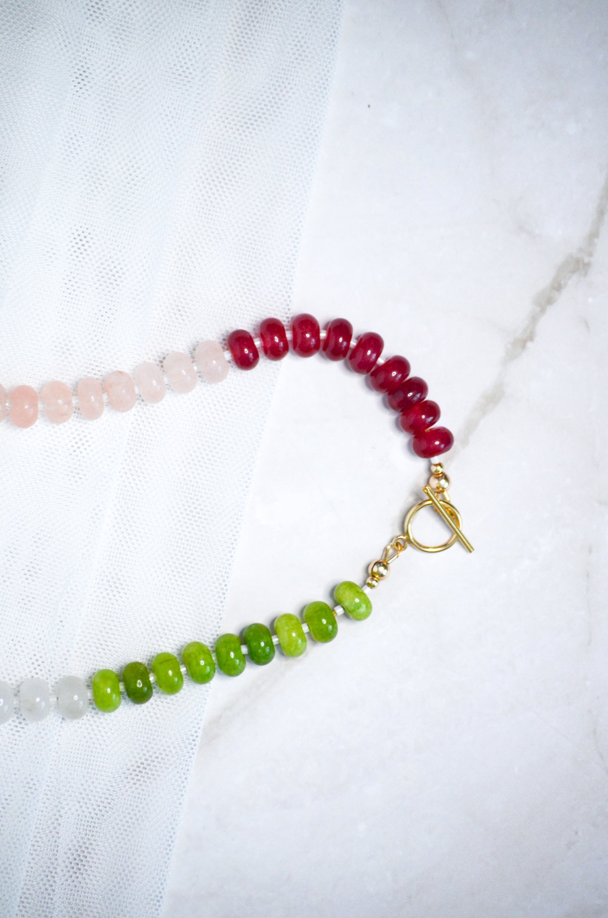 Beaded necklace with red, green, and a gold toggle clasp on a white background