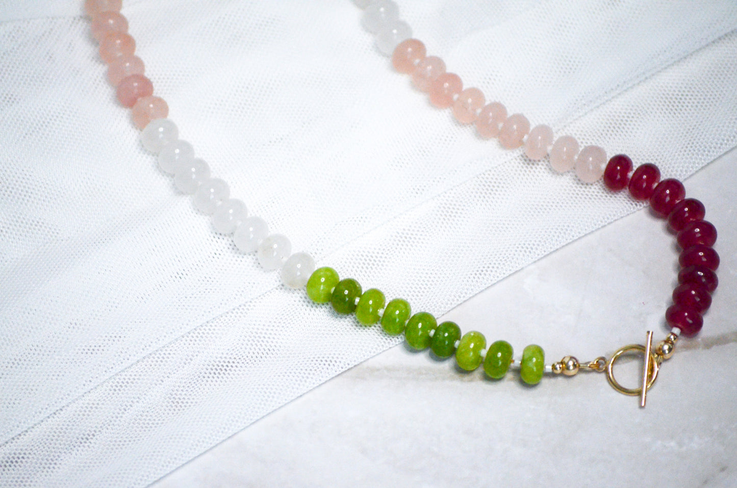 Necklace with multicolored beads and a gold toggle clasp on a white fabric background