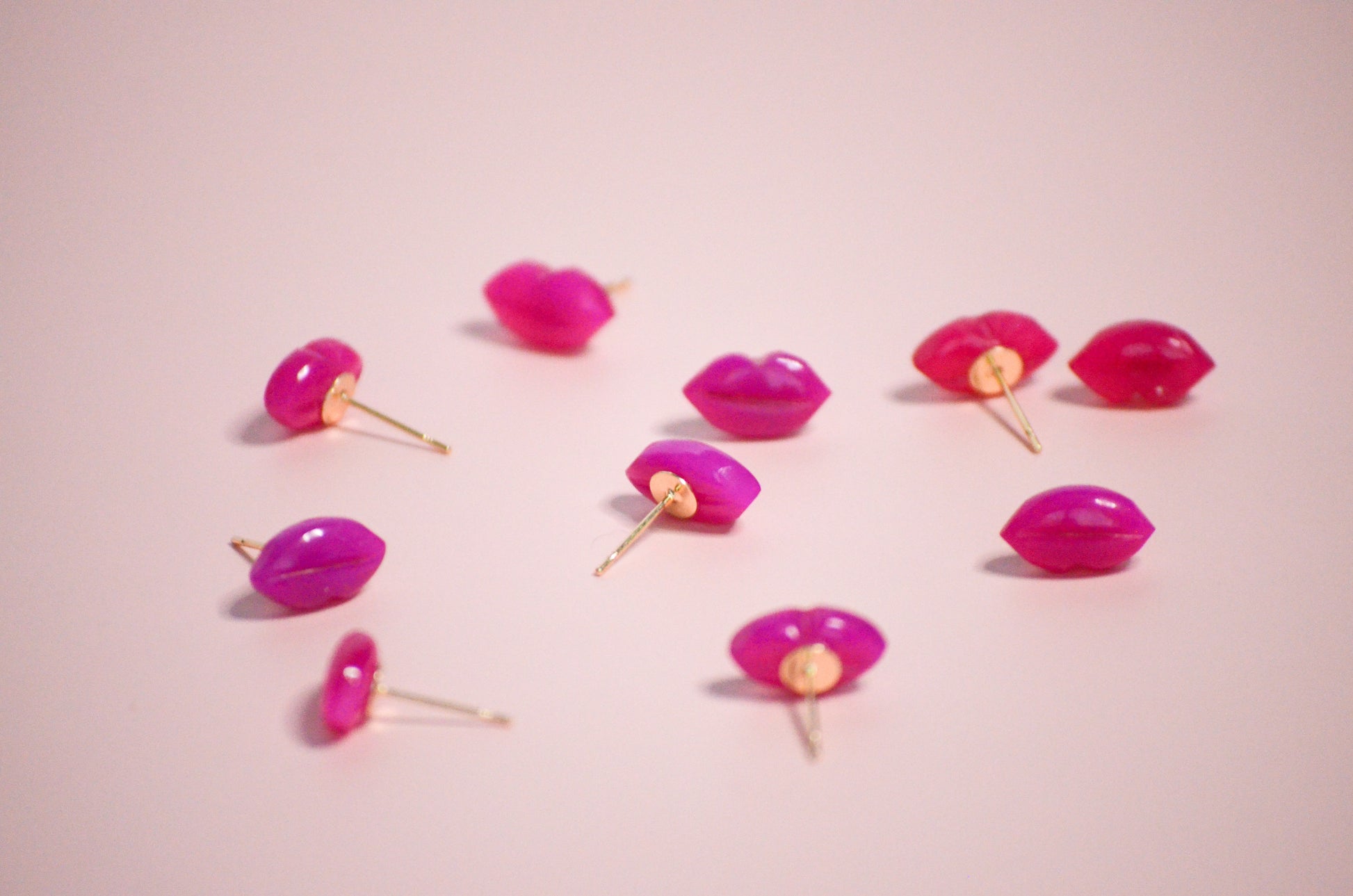 Pink lip-shaped with gold post earrings on a pink background