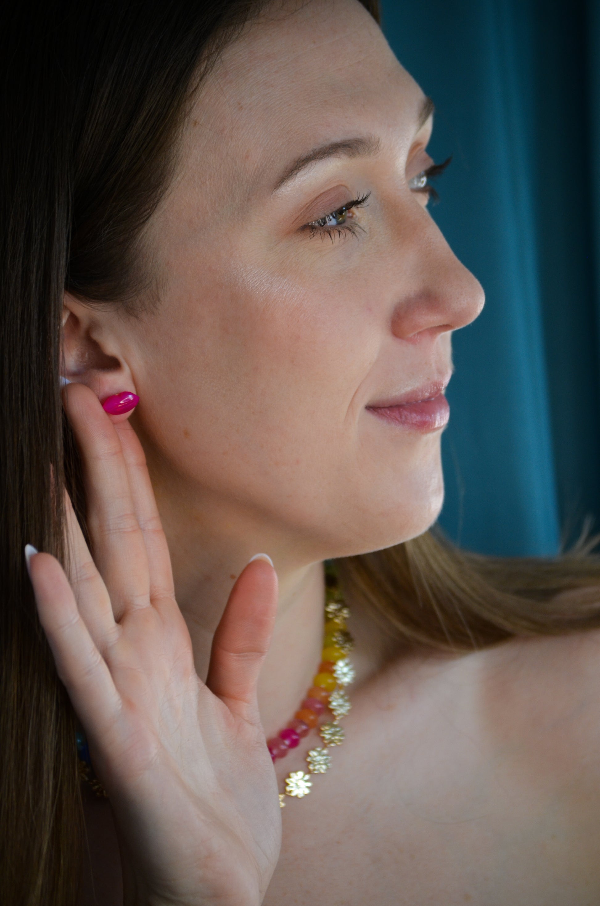 Woman wearing a colorful necklace and lip earrings with a blue curtain background