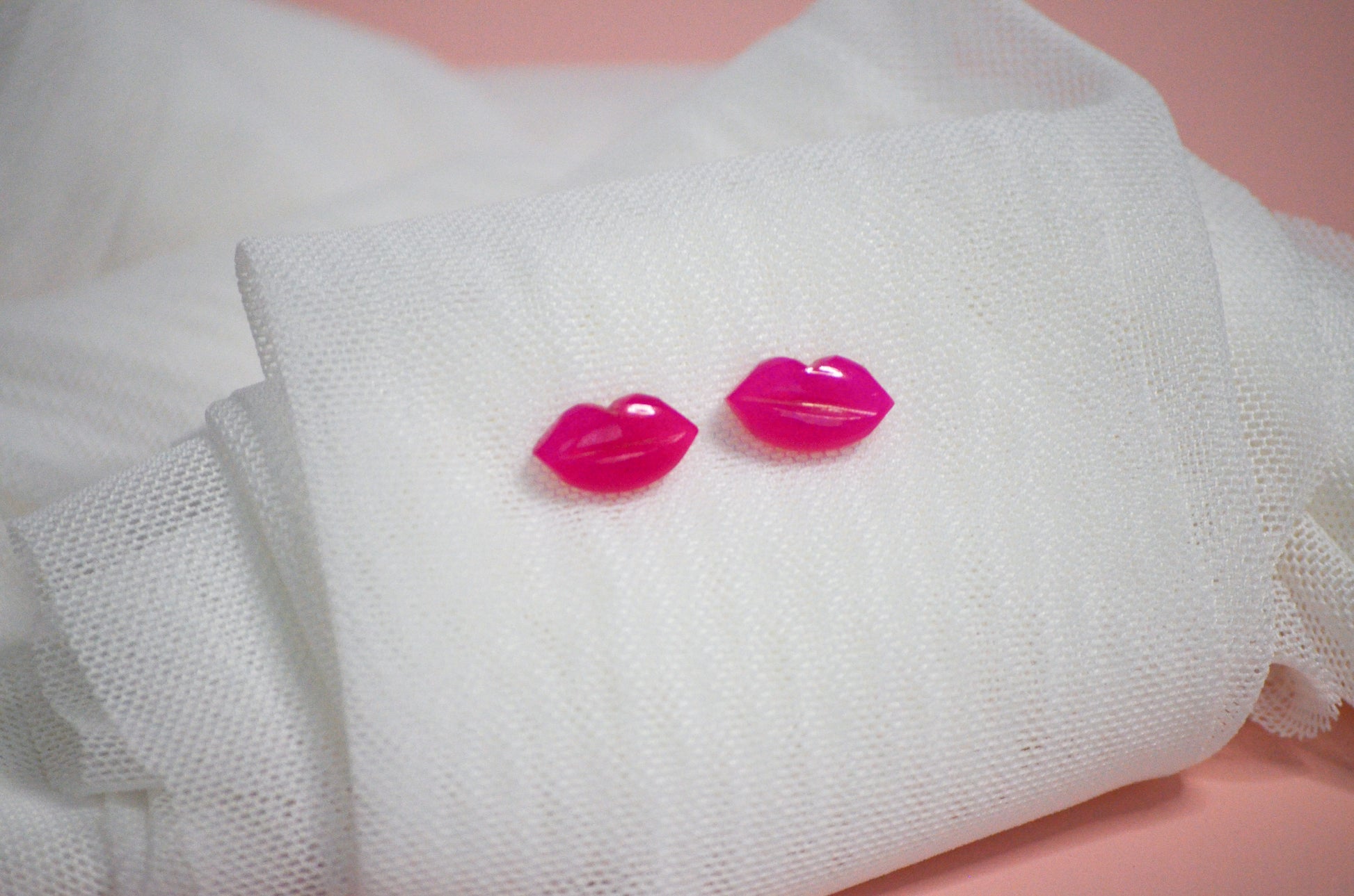 Pink lip-shaped earrings on a white fabric background