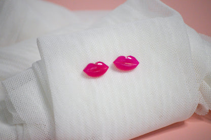 Pink lip-shaped earrings on a white fabric background