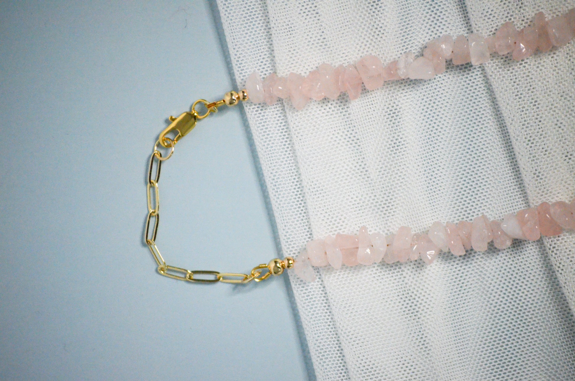 Necklace with pink gemstones and gold chain and clasp on a textured white surface