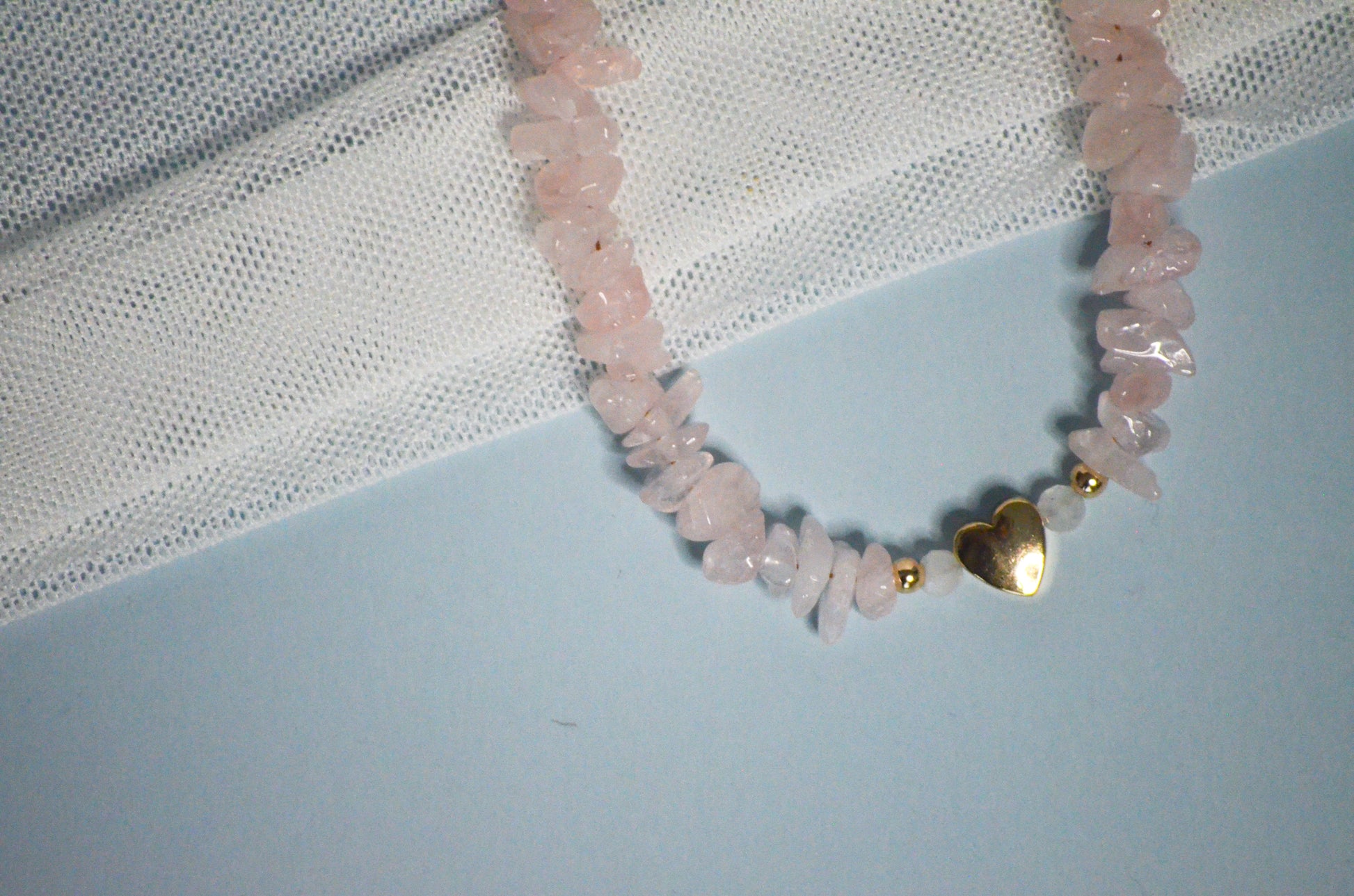 Necklace with pink beads and a gold heart charm on a light blue surface.