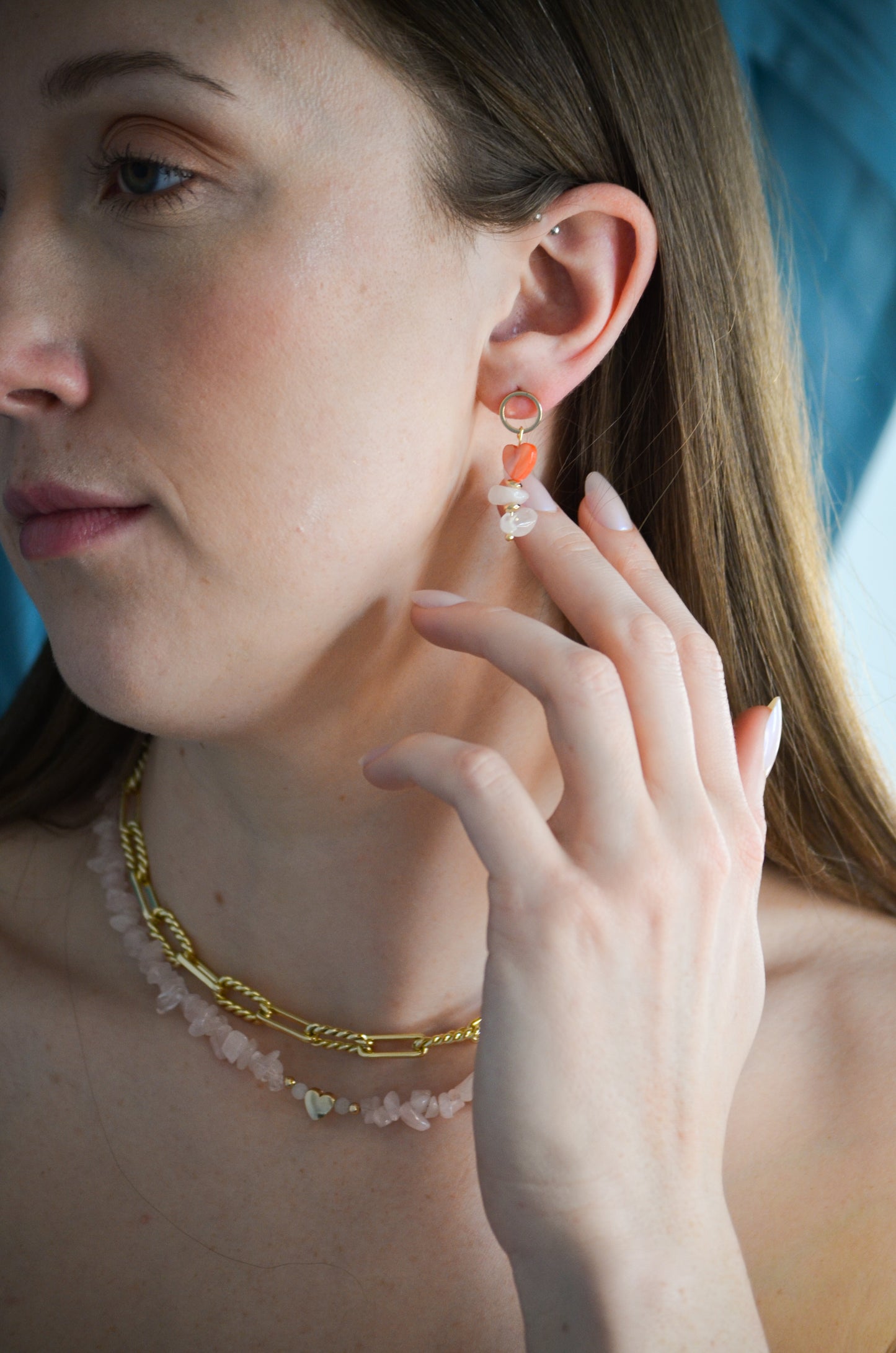 Close-up of a woman wearing earrings and a necklace, with a blurred background.