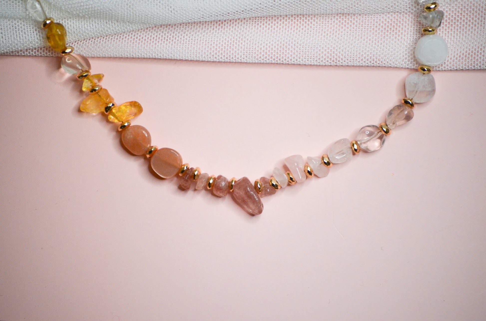 Necklace with multicolored warm toned and gold beads on a light pink background