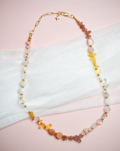 Necklace with multicolored warm toned and gold beads on a pink and white background