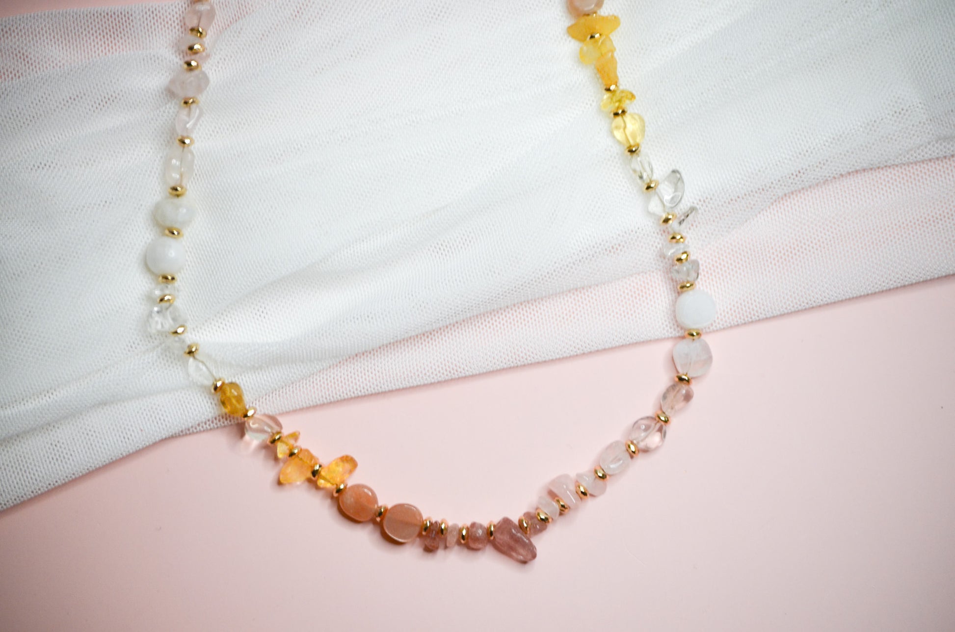 Necklace with warm toned and gold beads on a white and pink fabric background