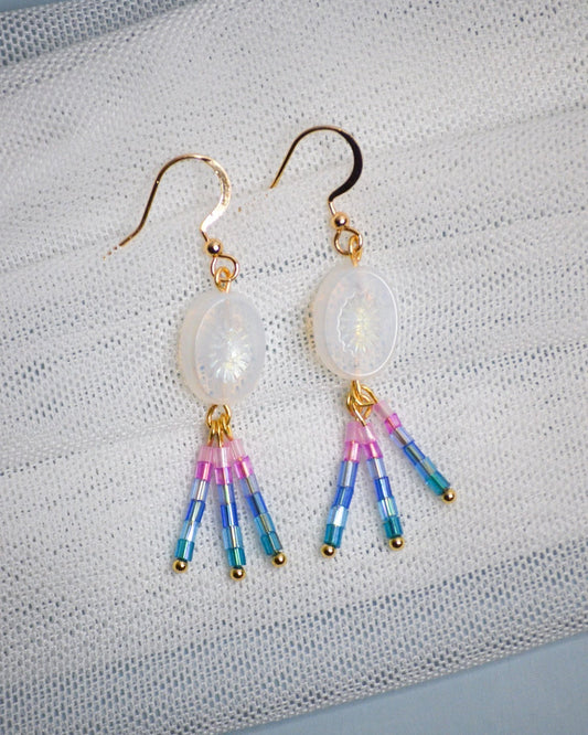Pair of earrings with colorful beads and iridescent gemstones on a textured fabric background