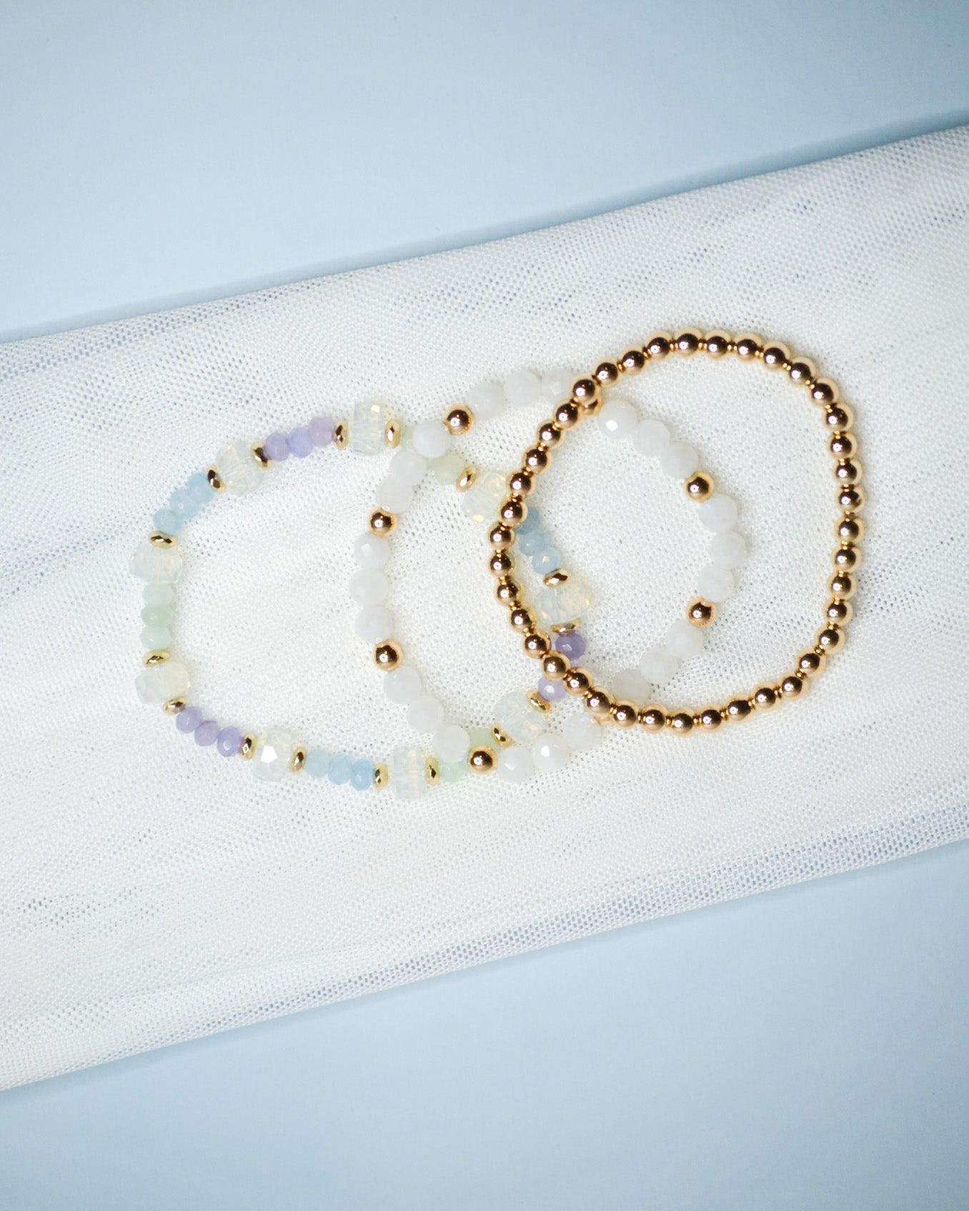 Three beaded iridescent and gold bracelets on a light blue background