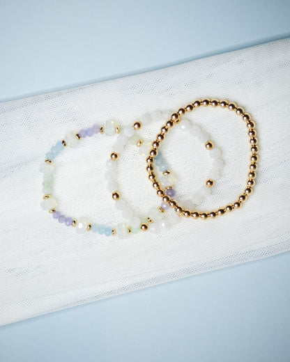 Three beaded iridescent and gold bracelets on a light blue background