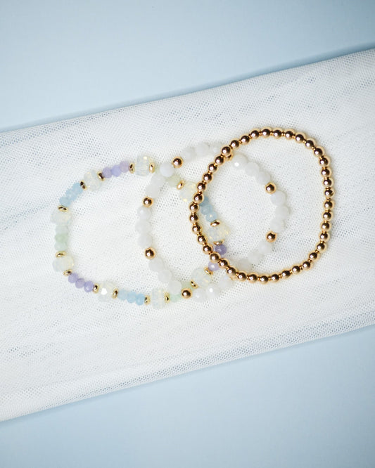 Three beaded iridescent and gold bracelets on a light blue background