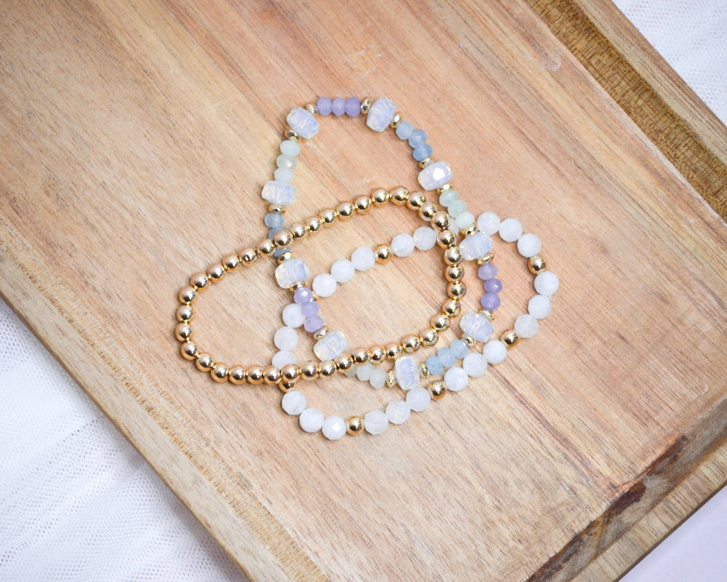 Three iridescent and gold beaded bracelets on a wooden surface