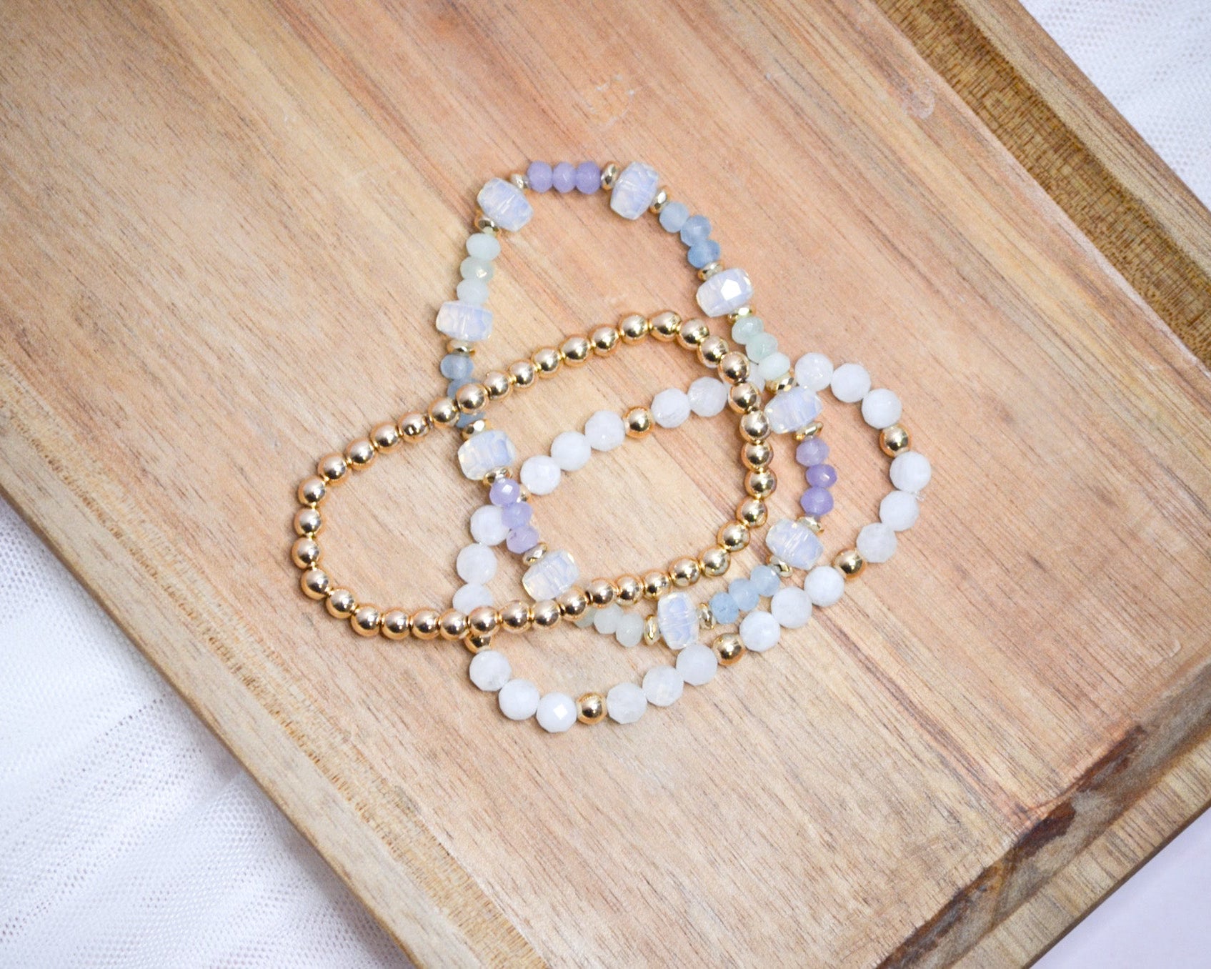 Three iridescent and gold beaded bracelets on a wooden surface