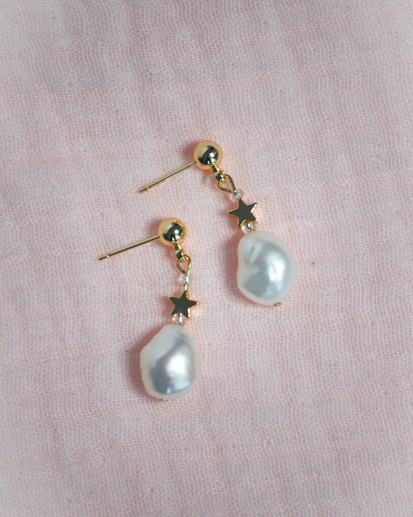 Pearl earrings with gold accents on a pink background