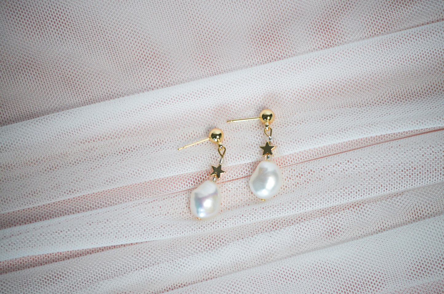 Pearl earrings with gold star accents on a textured fabric background