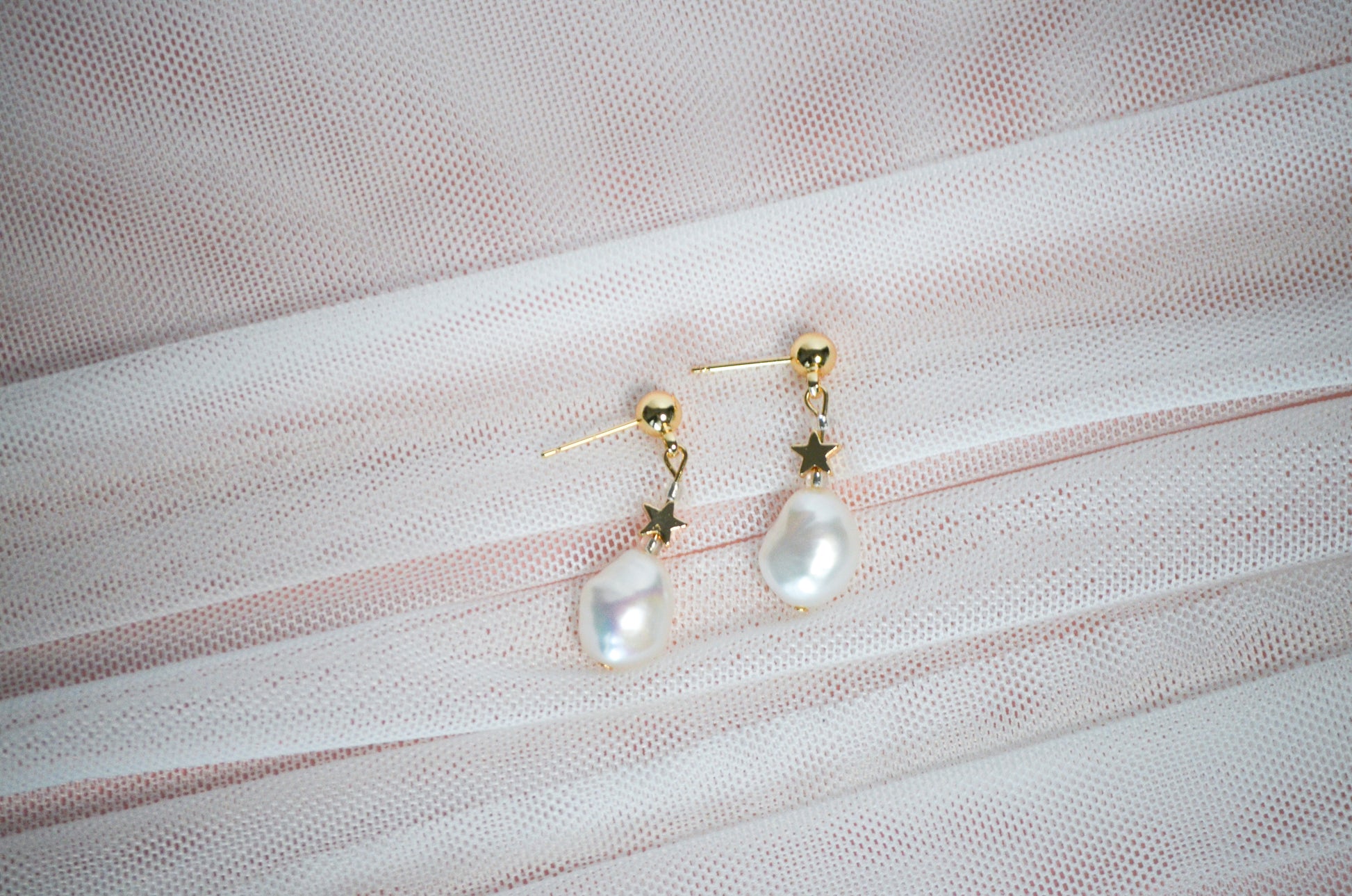 Pearl earrings with gold star accents on a textured fabric background