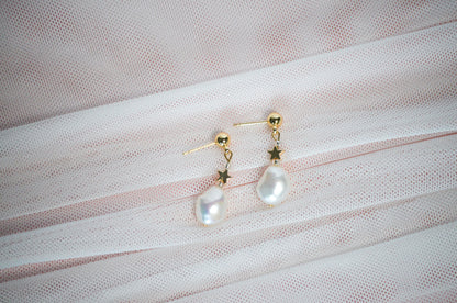 Pearl earrings with gold star accents on a textured fabric background