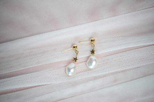 Pearl earrings with gold star accents on a textured fabric background