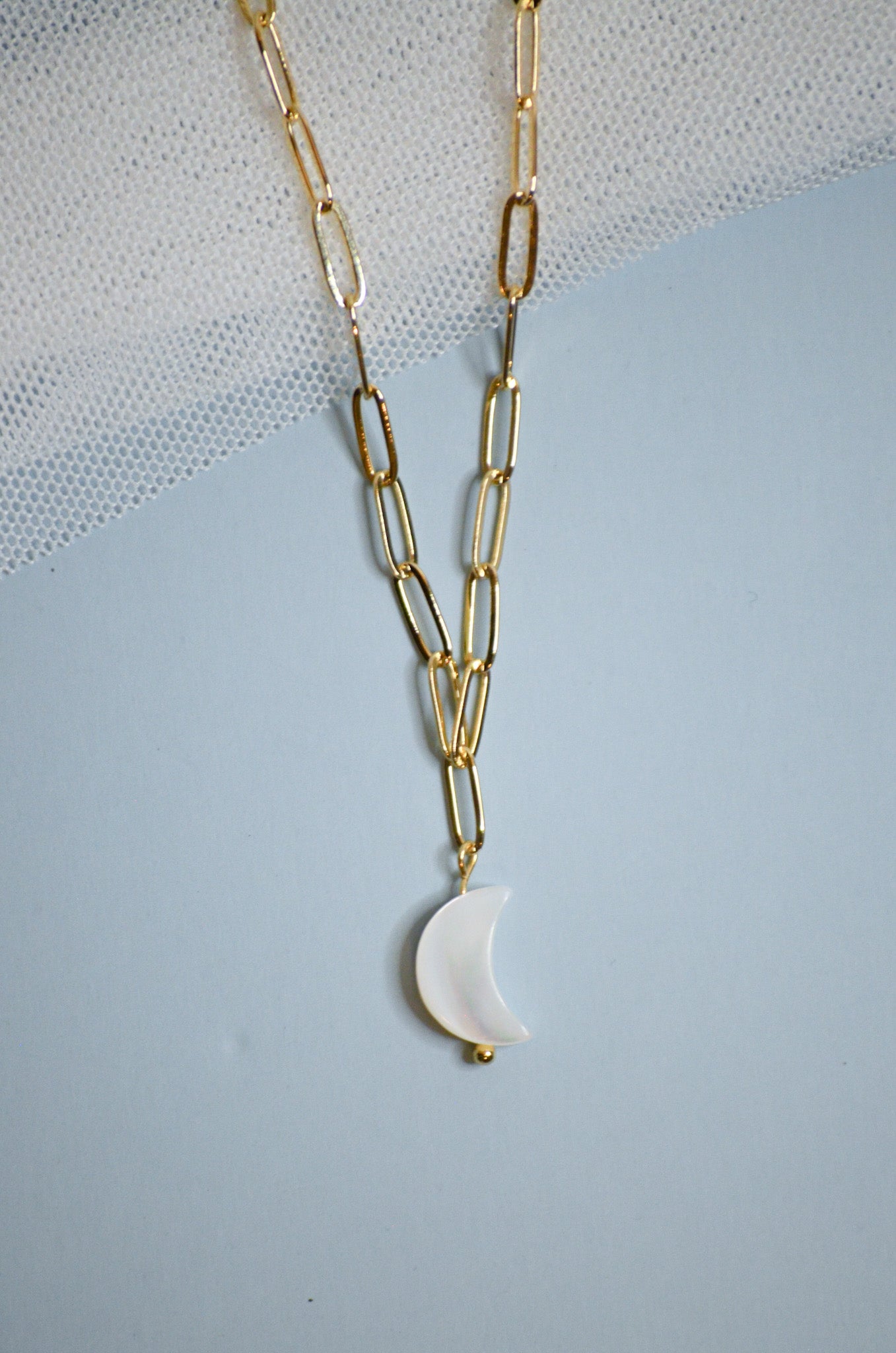 Gold chain necklace with a white mother of pearl crescent moon pendant on a light blue background