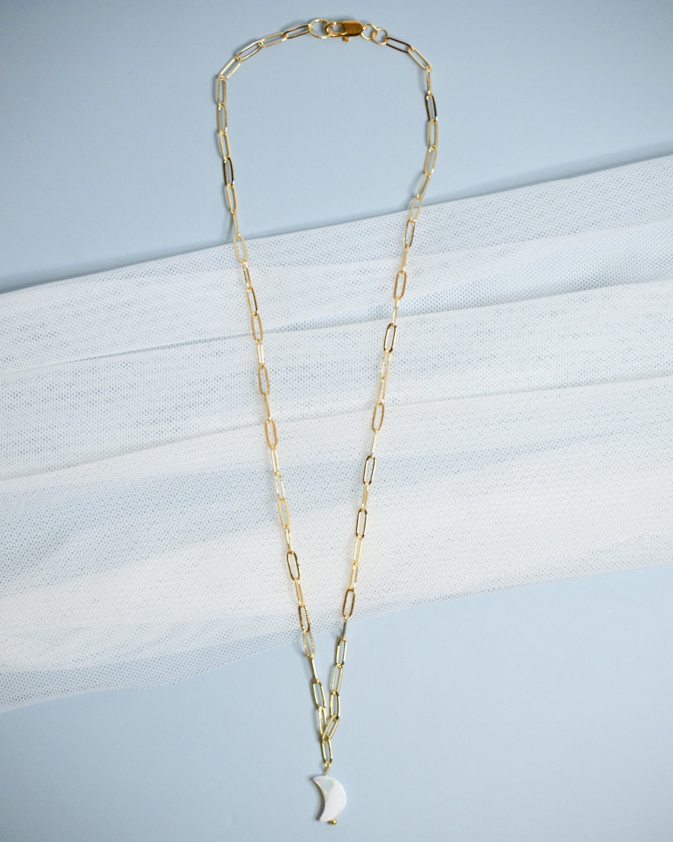 Gold chain necklace with a moon-shaped mother of pearl pendant on a light blue background
