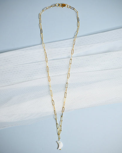Gold chain necklace with a moon-shaped mother of pearl pendant on a light blue background