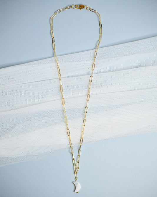 Gold chain necklace with a moon-shaped mother of pearl pendant on a light blue background