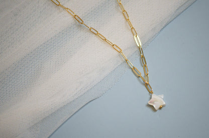 Gold chain necklace with a mother of pearl star-shaped pendant on a textured fabric background
