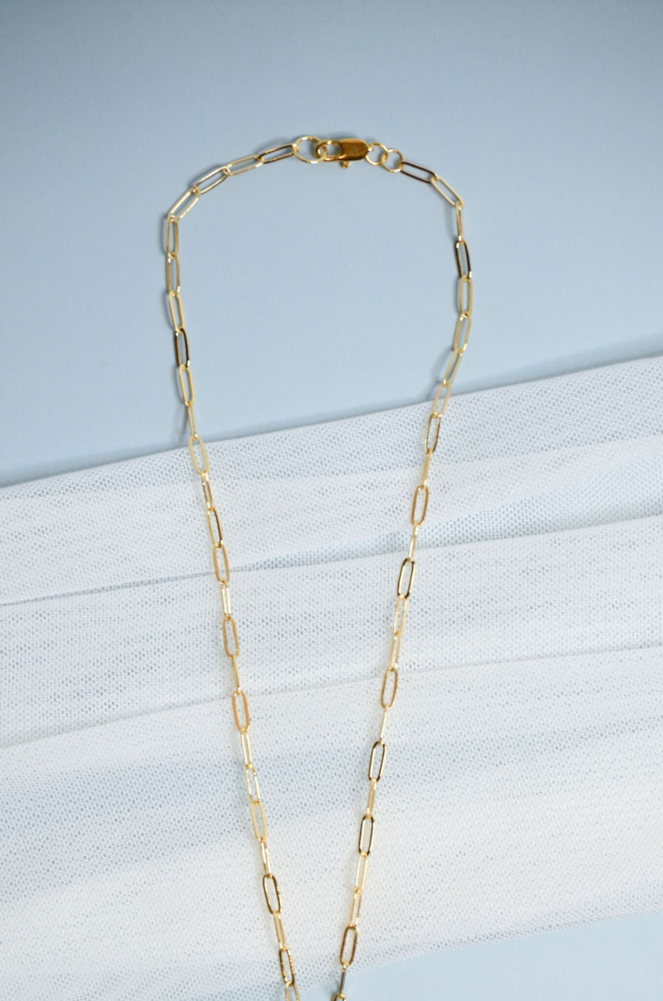Gold chain necklace on a light blue and white striped background