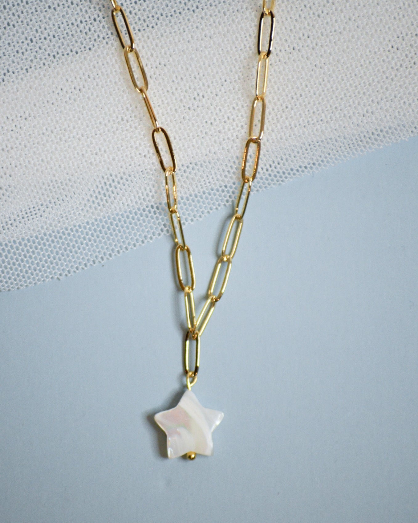 Gold chain necklace with a star-shaped mother of pearl pendant on a light blue background