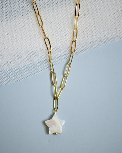 Gold chain necklace with a star-shaped mother of pearl pendant on a light blue background