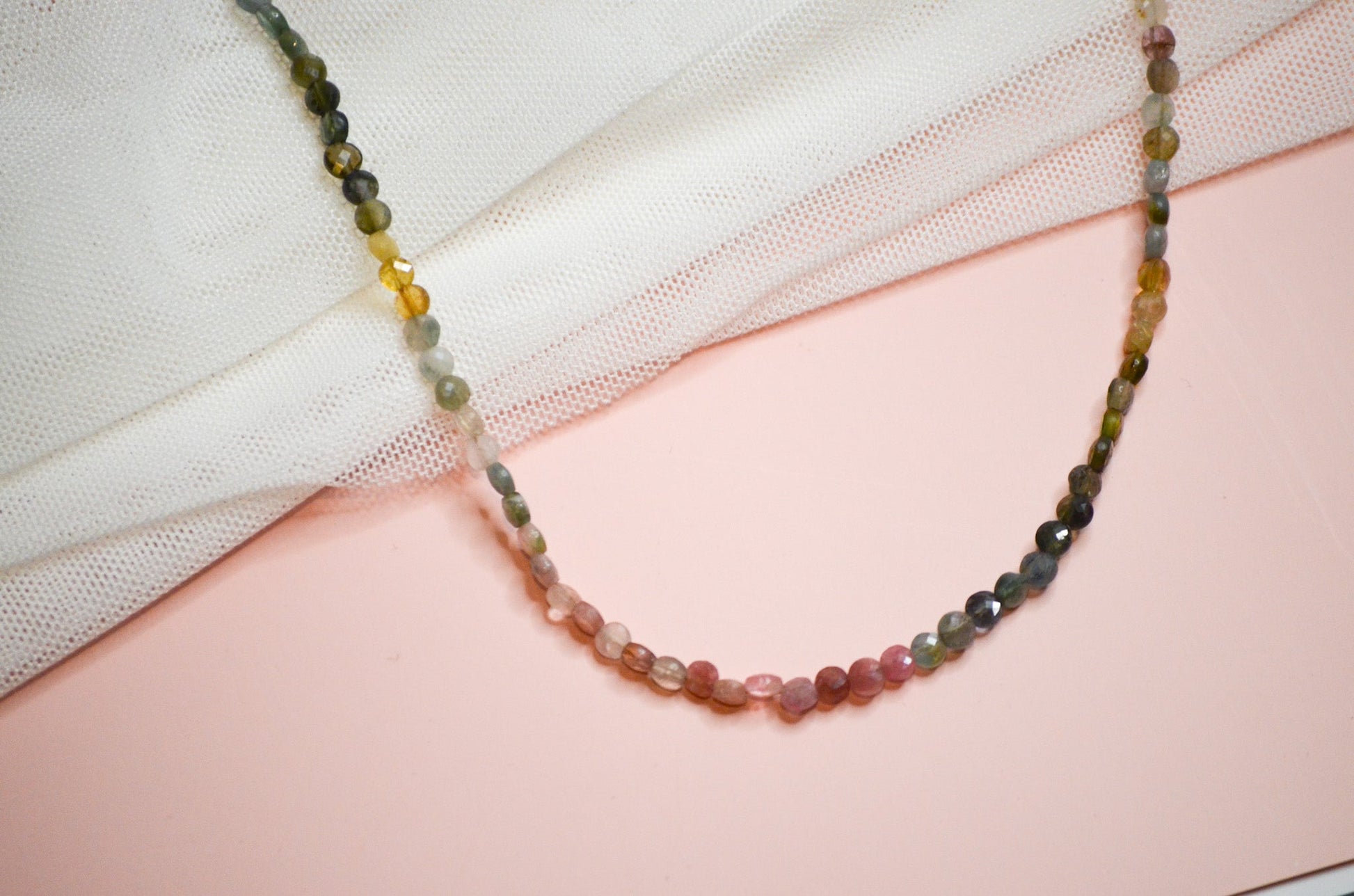 Multicolored green, pink, and yellow beaded necklace on a pink and white fabric background