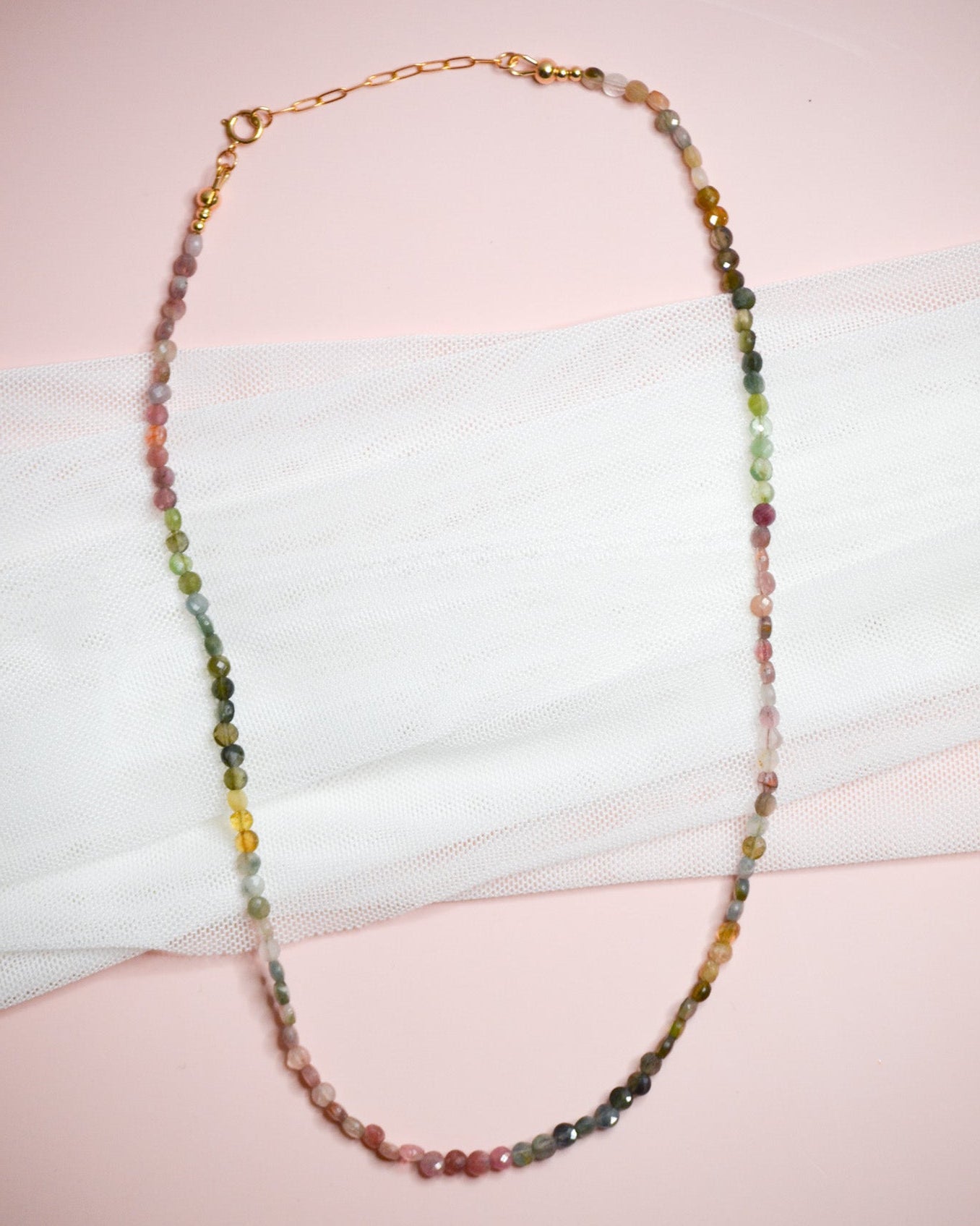 Multicolored green, pink, and yellow beaded necklace on a white surface with a pink background
