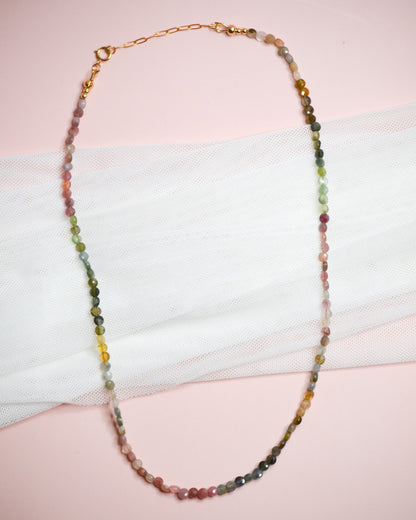 Multicolored green, pink, and yellow beaded necklace on a white surface with a pink background