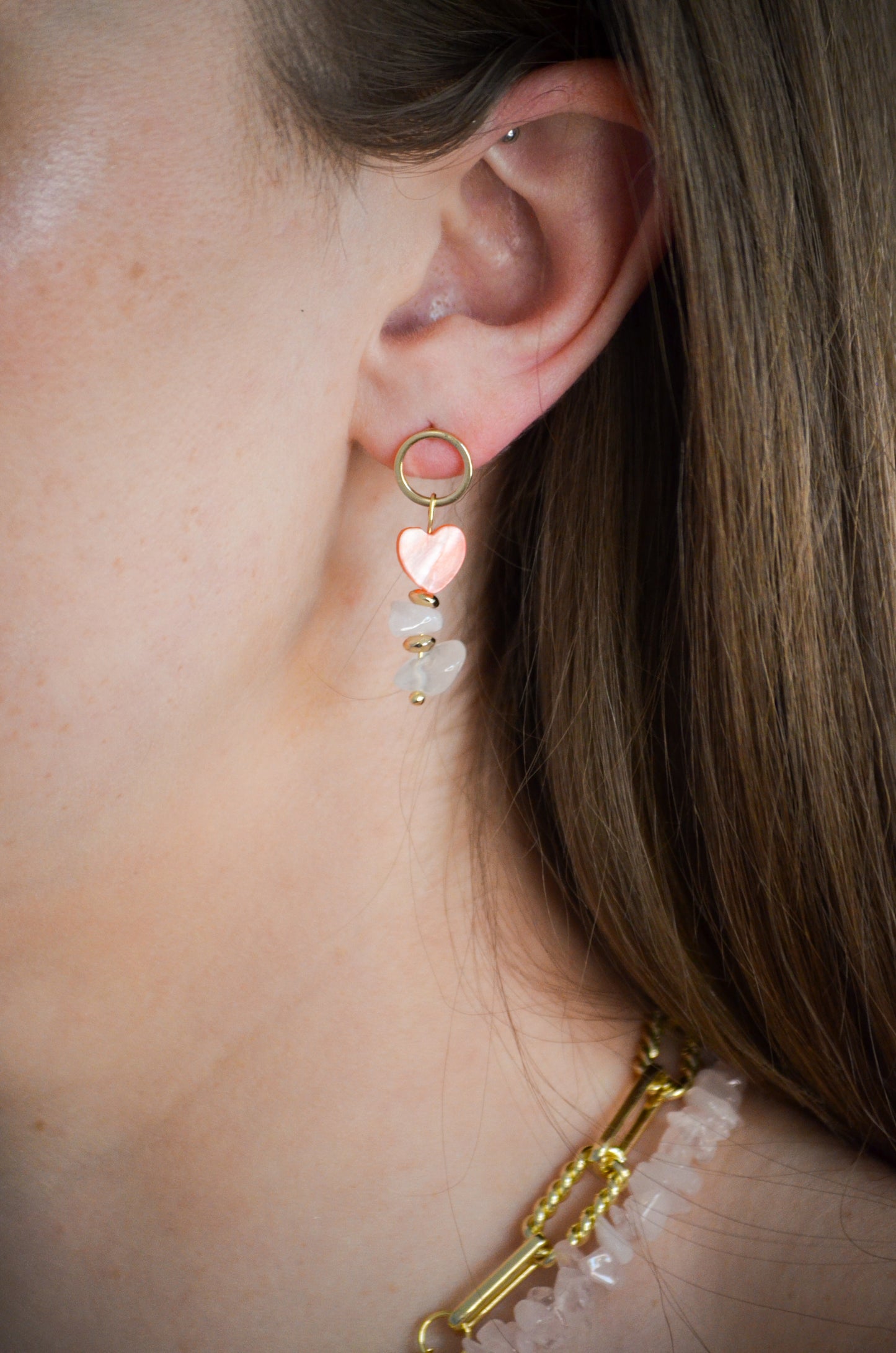 Close-up of a person wearing a gold earring with heart-shaped charms.