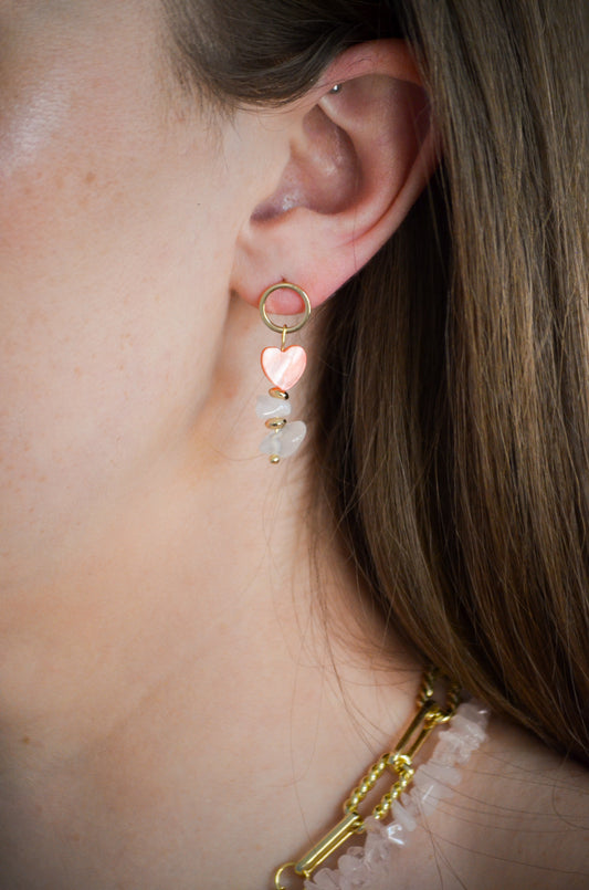 Close-up of a person wearing a gold earring with heart-shaped charms.